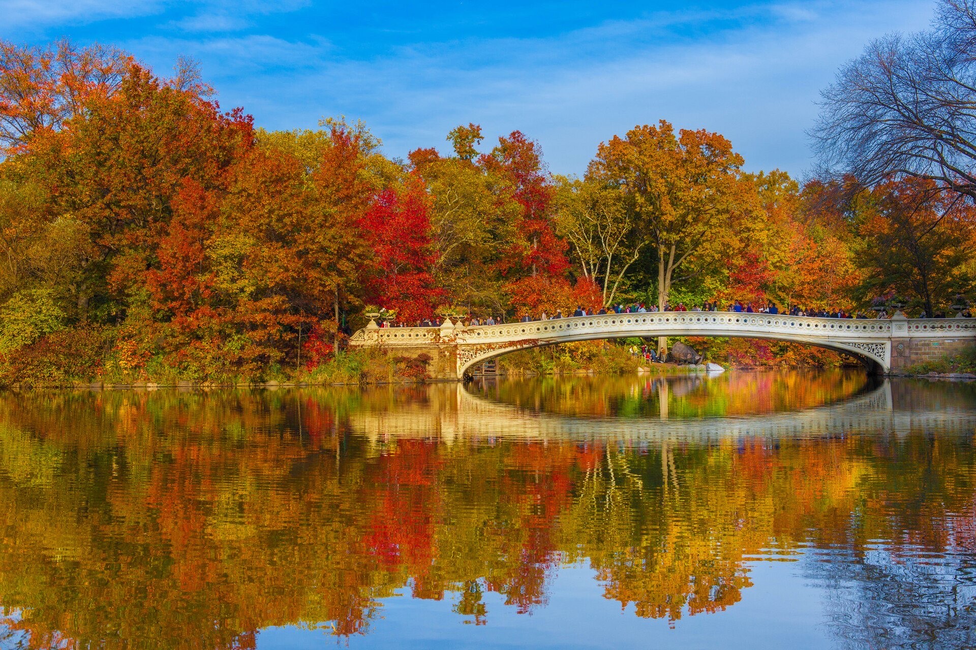 Bow Bridge in Central Park, New York, framed by red and orange autumn foliage reflected in the lake