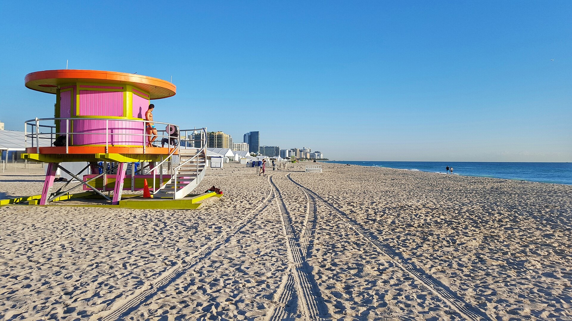 Pink and white lifeguard tower on the wide sand of South Beach, Miami Beach, with the skyline behind