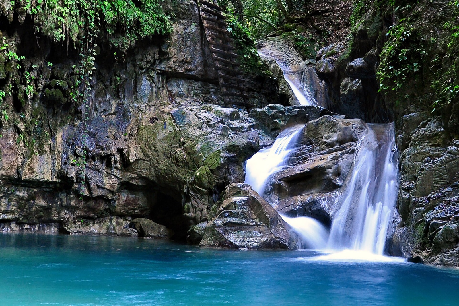 A waterfall falling into a turquoise pool between striated rock walls at Damajagua, Dominican Republic