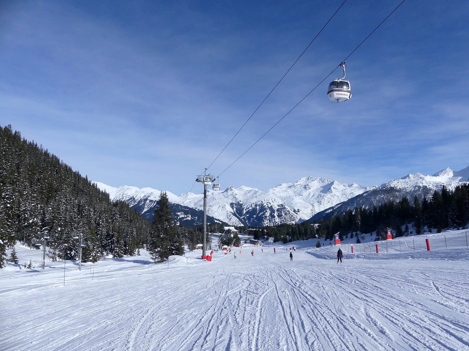 A groomed ski run descending towards Courchevel 1850 in December, with a gondola line and snow-covered peaks behind