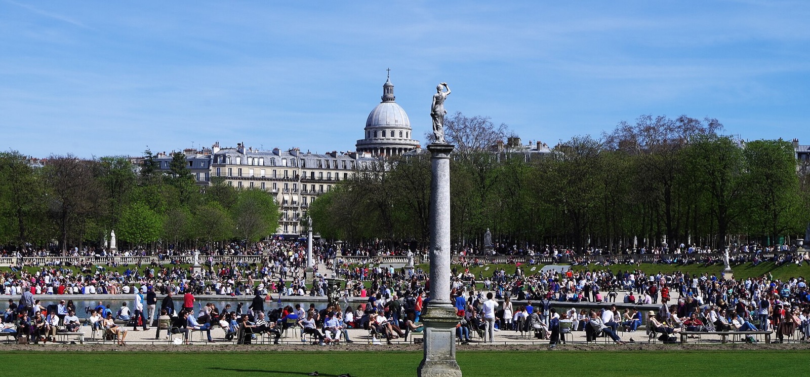 Parisians sitting around the pond in the Jardin du Luxembourg on a spring day, with the dome of the Pantheon behind