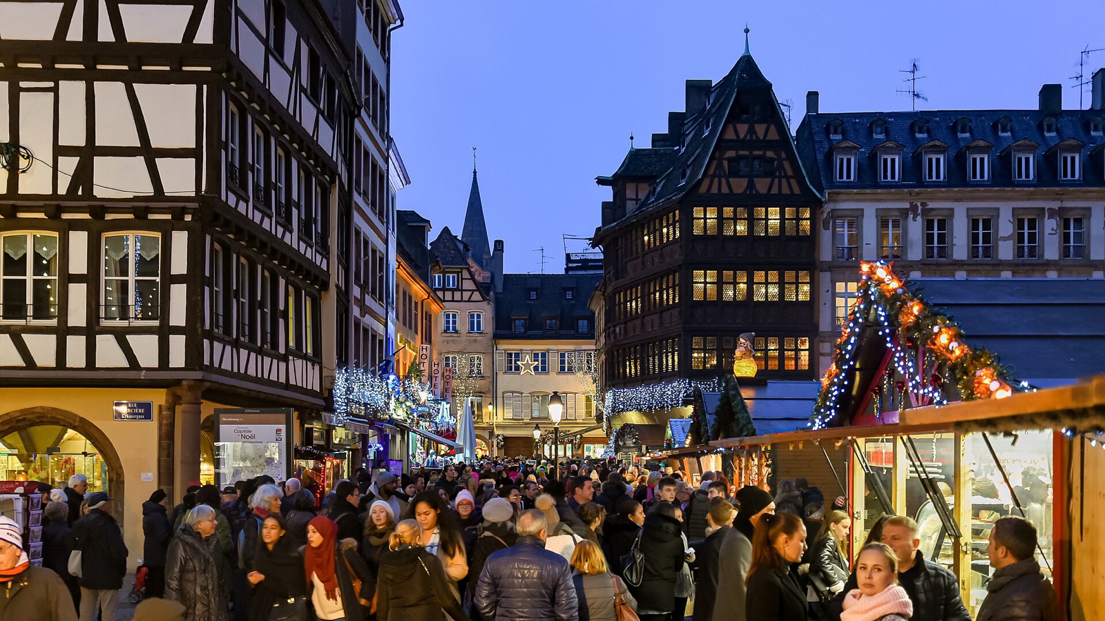 Crowds under Christmas lights between half-timbered houses at the Strasbourg Christmas market at dusk
