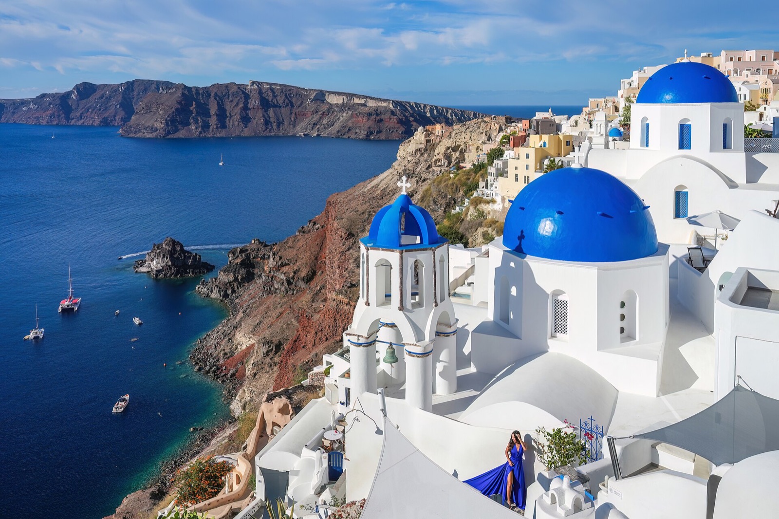 The three blue domes of Oia on Santorini, seen above the caldera with the sea and the cliff behind