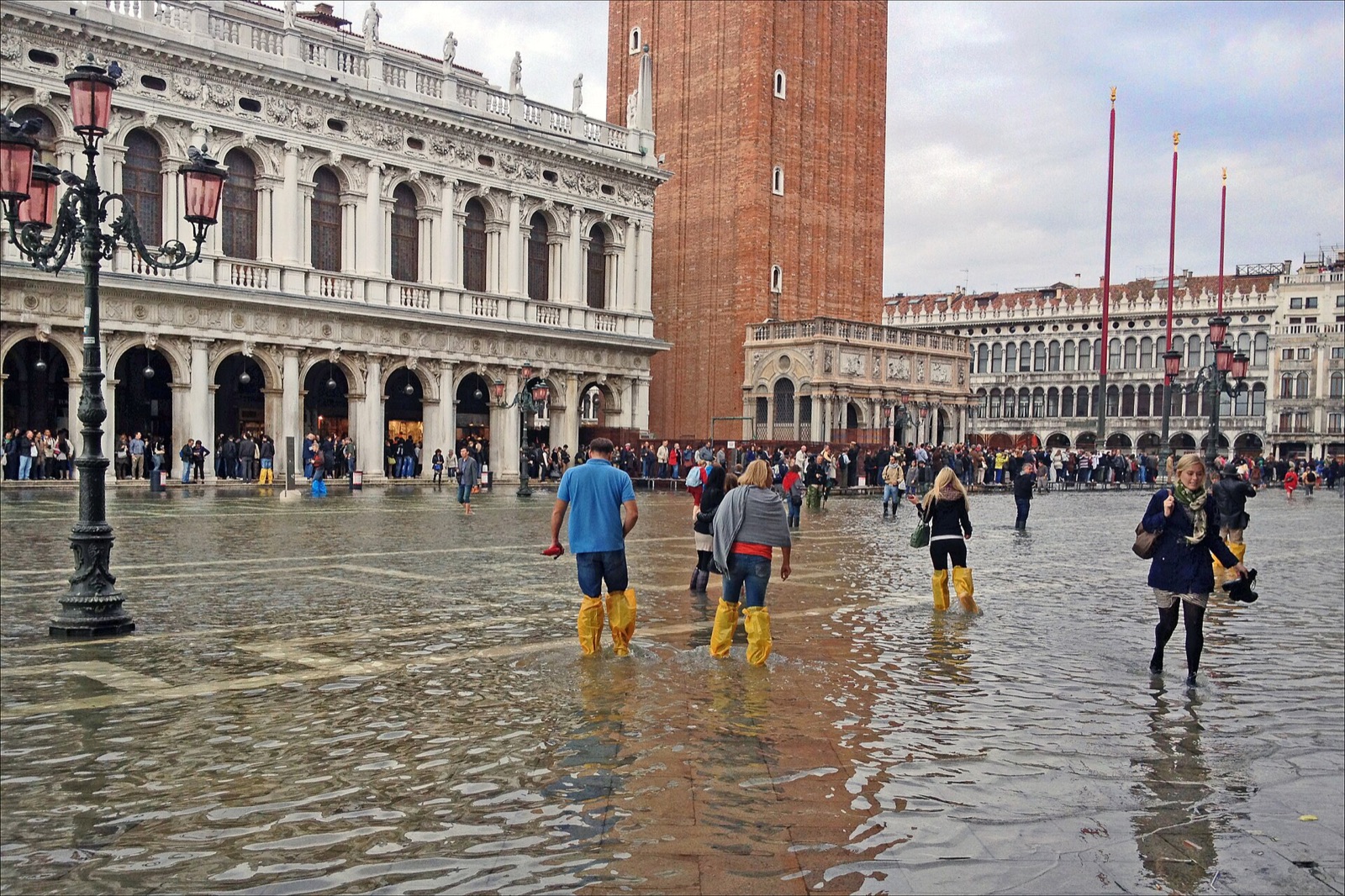Acqua alta in St Mark's Square in Venice, with visitors in boots walking through shallow floodwater in front of the basilica