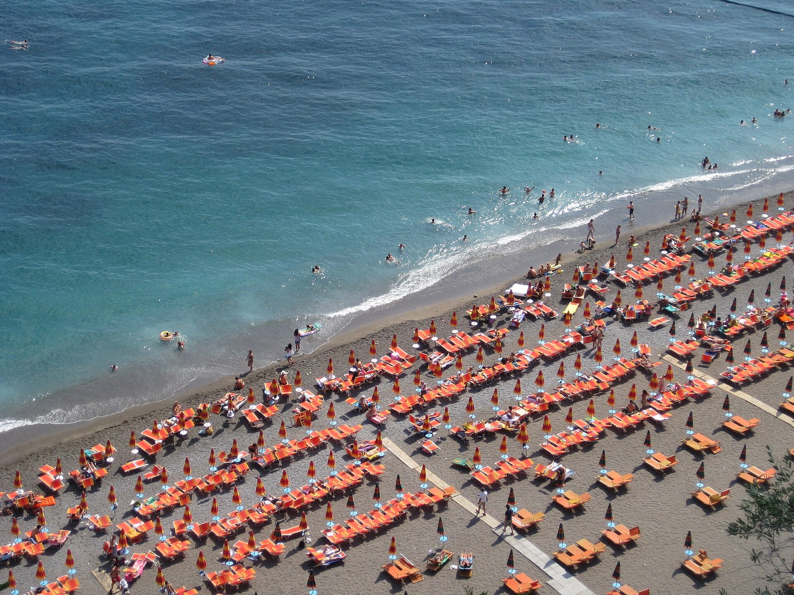 The beach at Positano on the Amalfi Coast seen from above, packed with orange sun umbrellas in rows