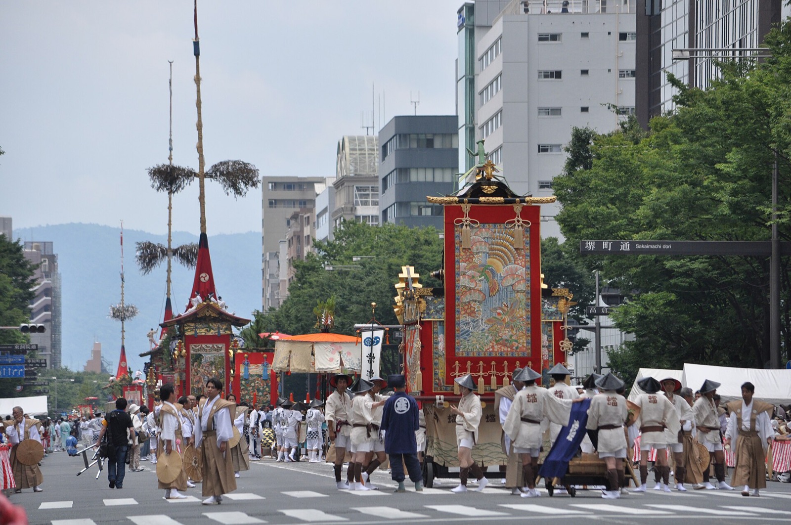 A tall wooden festival float with banners being pulled through a Kyoto street during the Gion Matsuri