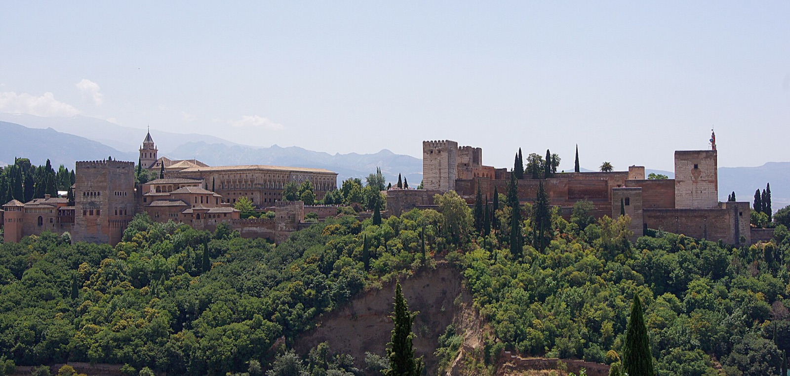 The Alhambra of Granada seen from the Mirador de San Nicolas, its red towers above wooded slopes