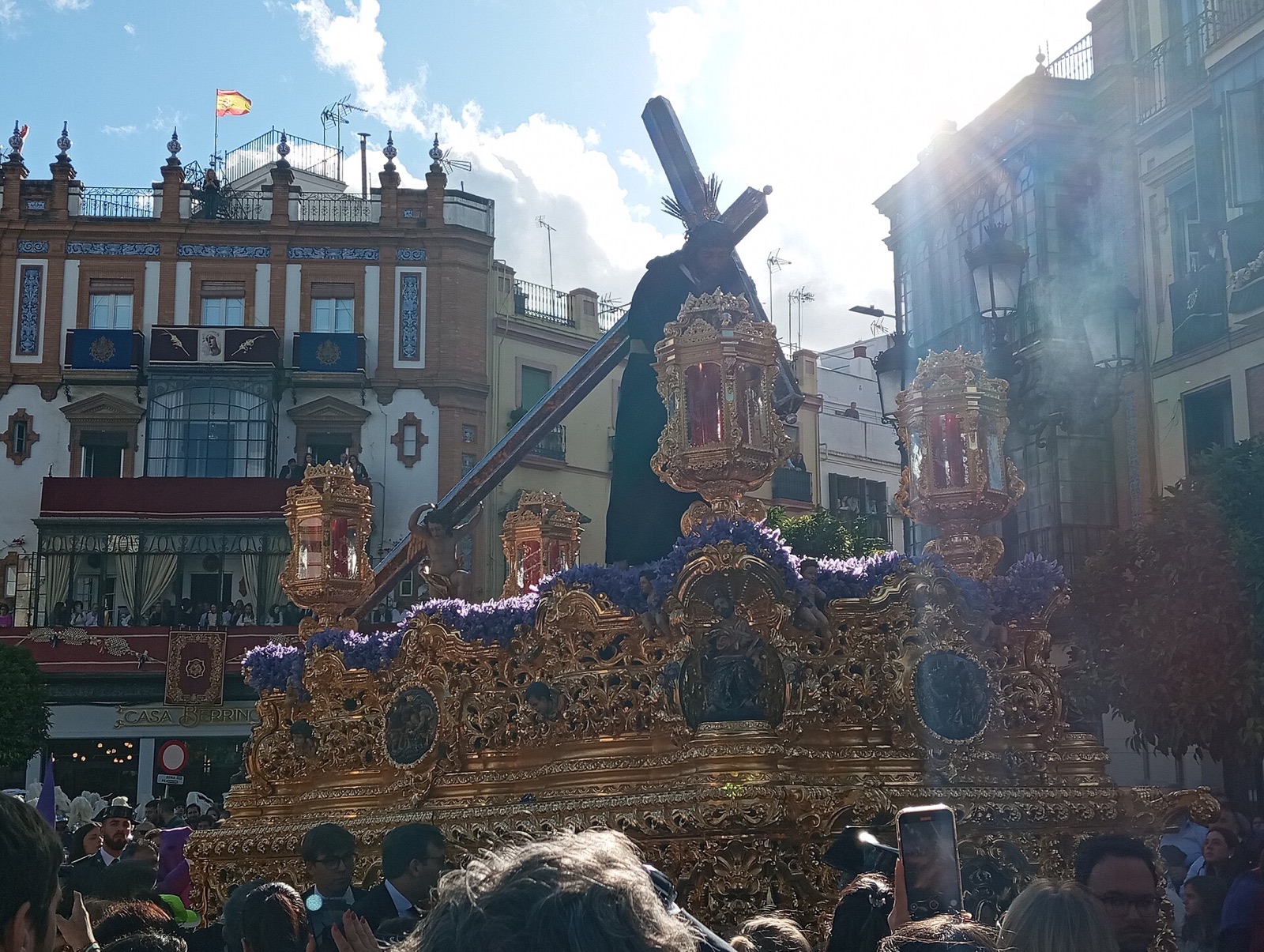 A Semana Santa paso carried through a Seville street during Holy Week, with crowds along the route
